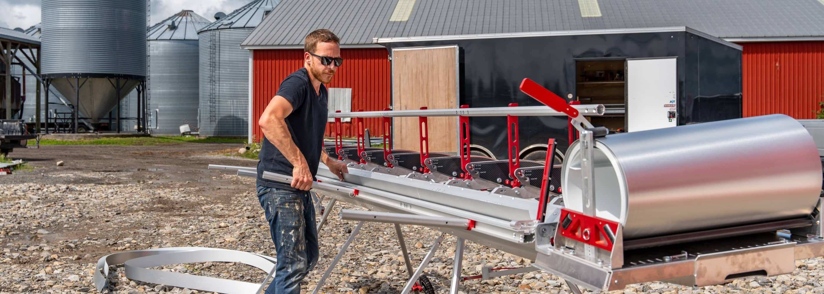 Innovatools modular siding brake user bending aluminum sheet in front of a red barn on a farm
